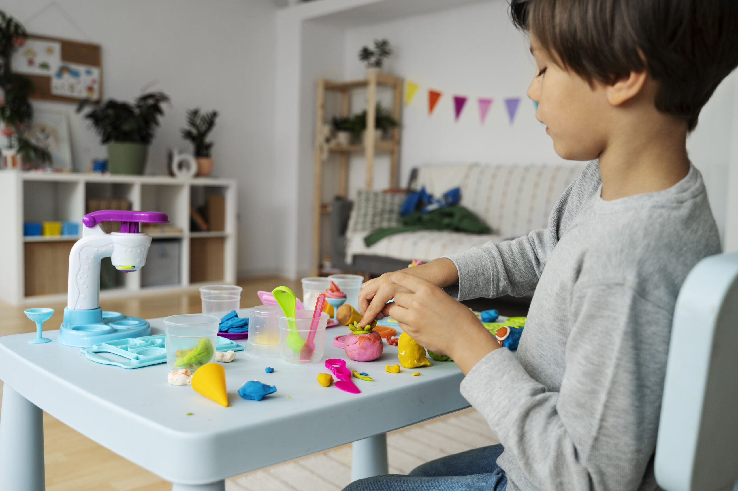 Young child engaged in creative pretend play with colorful modeling clay and toy kitchen accessories at home. The playful setup highlights how imaginative toys from MyToyShop help children develop creativity, problem-solving skills, fine motor abilities, and independent thinking through hands-on learning experiences.