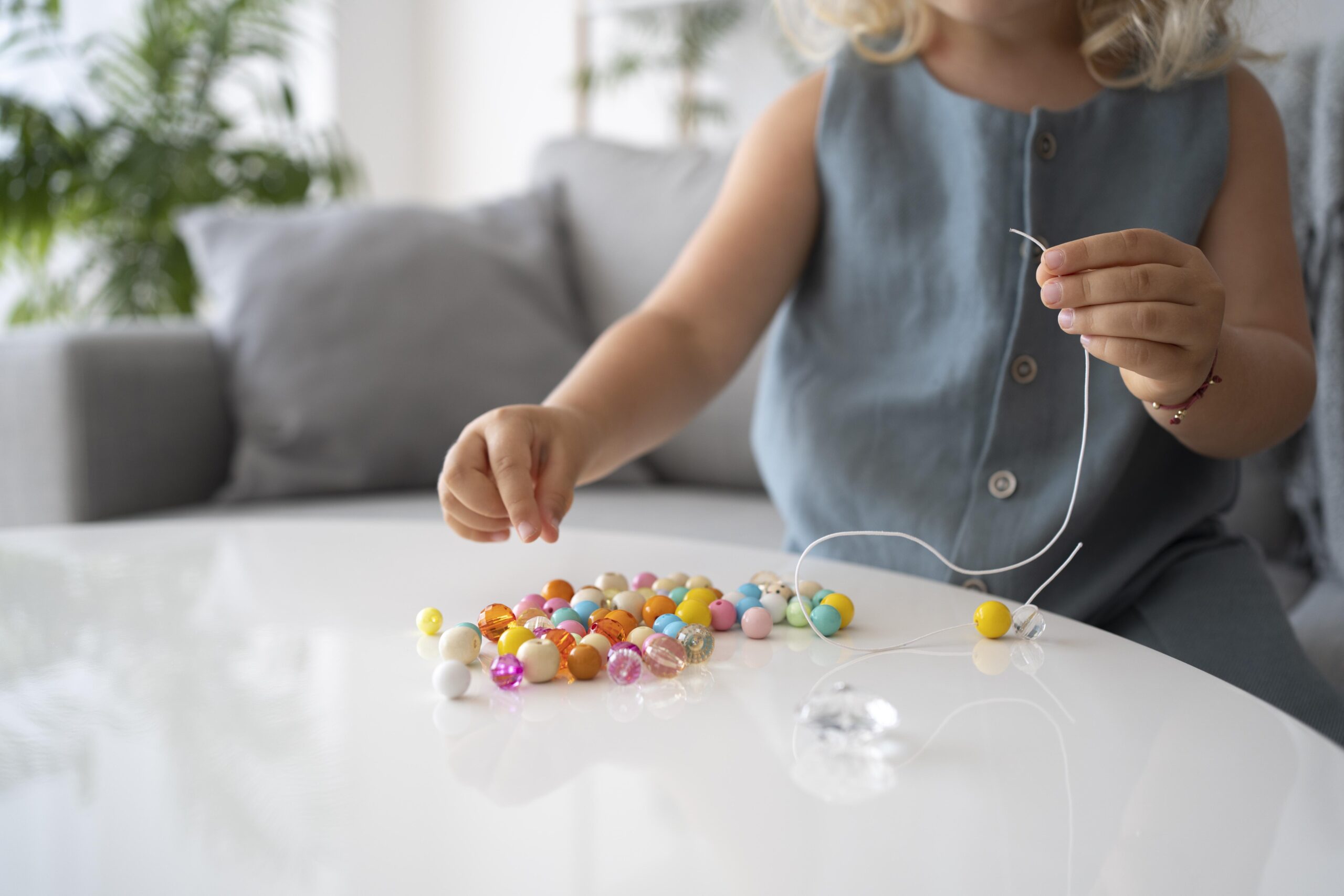 Child practising fine motor skills by threading colourful beads onto a string at home.